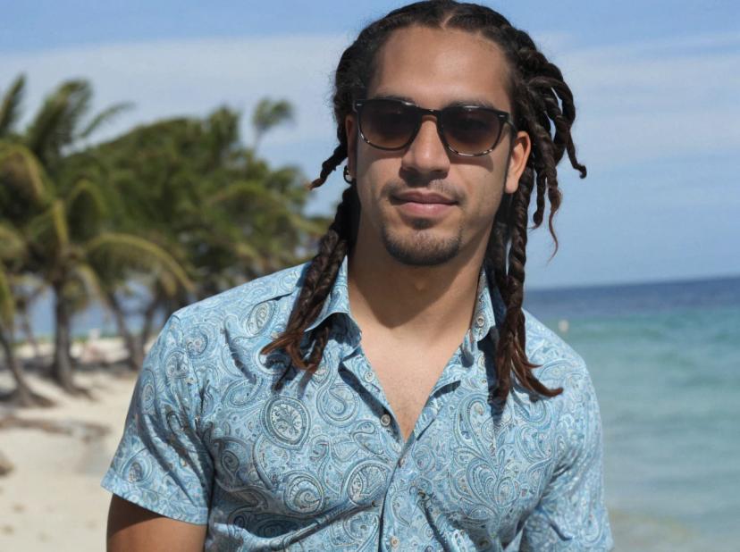 wide portrait photo of a latino man with dreadlocks on a beach, wearing a paisley shirt and sunglasses, palm trees and sea in the background
