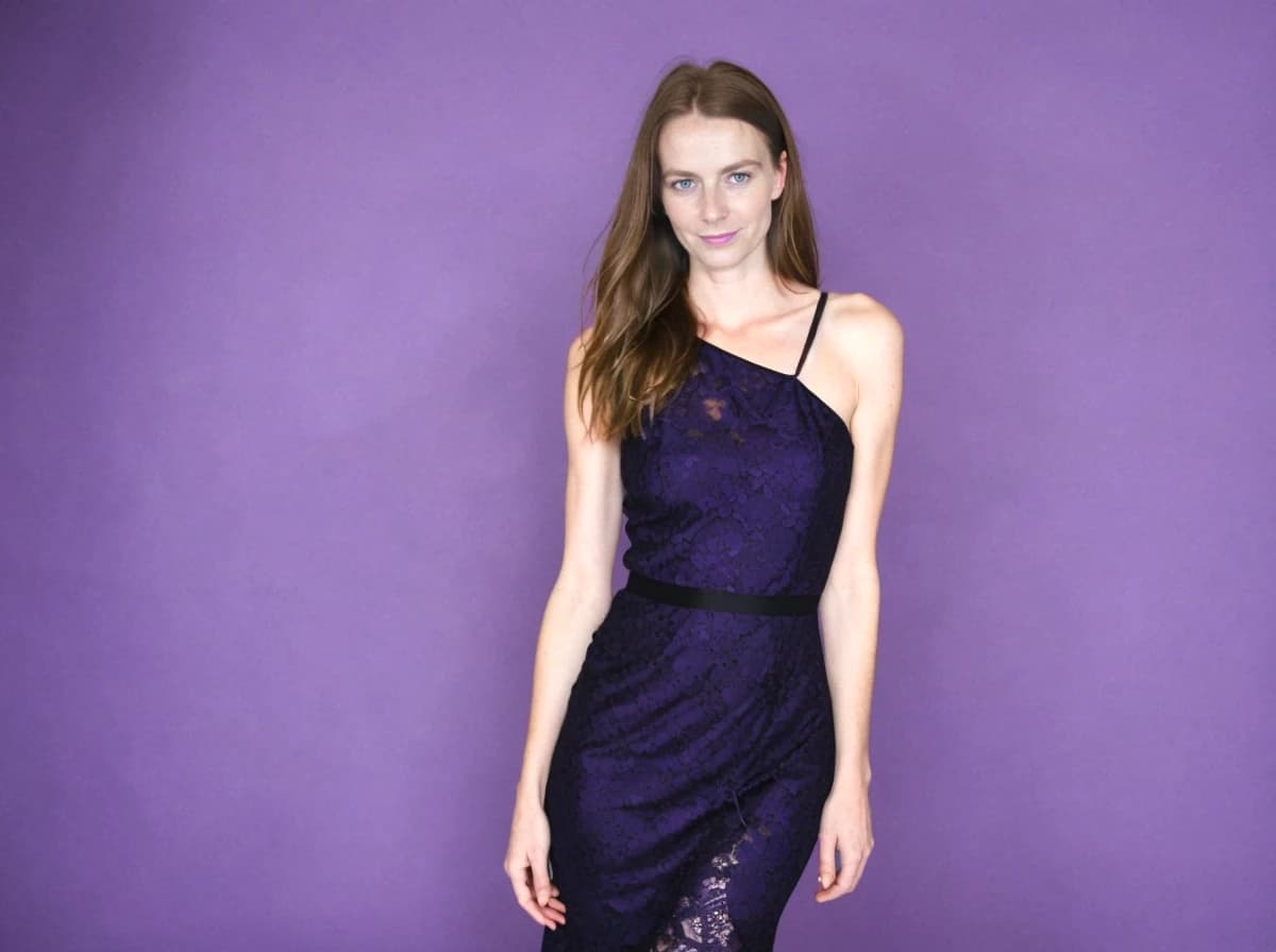 A woman wearing a one-shoulder navy blue lace dress with a black belt, standing against a purple background.