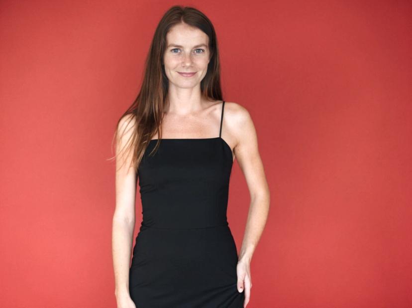 A woman wearing a black sleeveless dress standing against a red background.