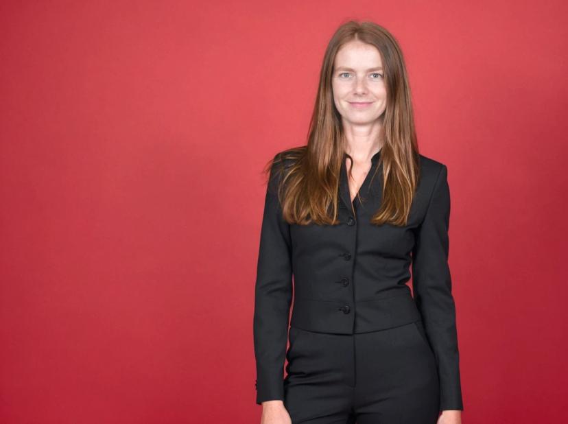 A woman wearing a black suit standing against a red background.