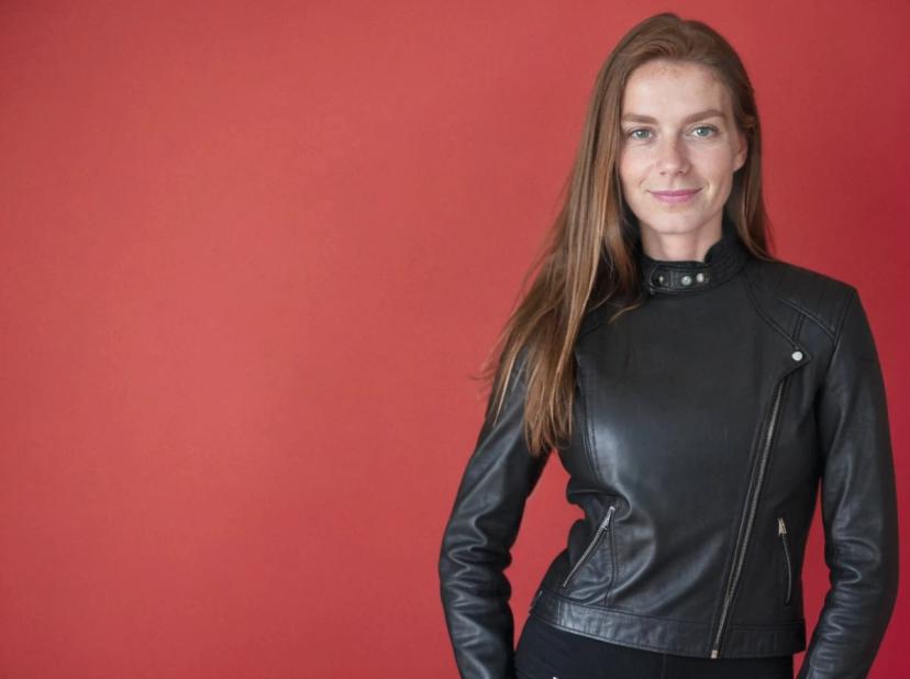 A woman wearing a black leather jacket standing against a red background.