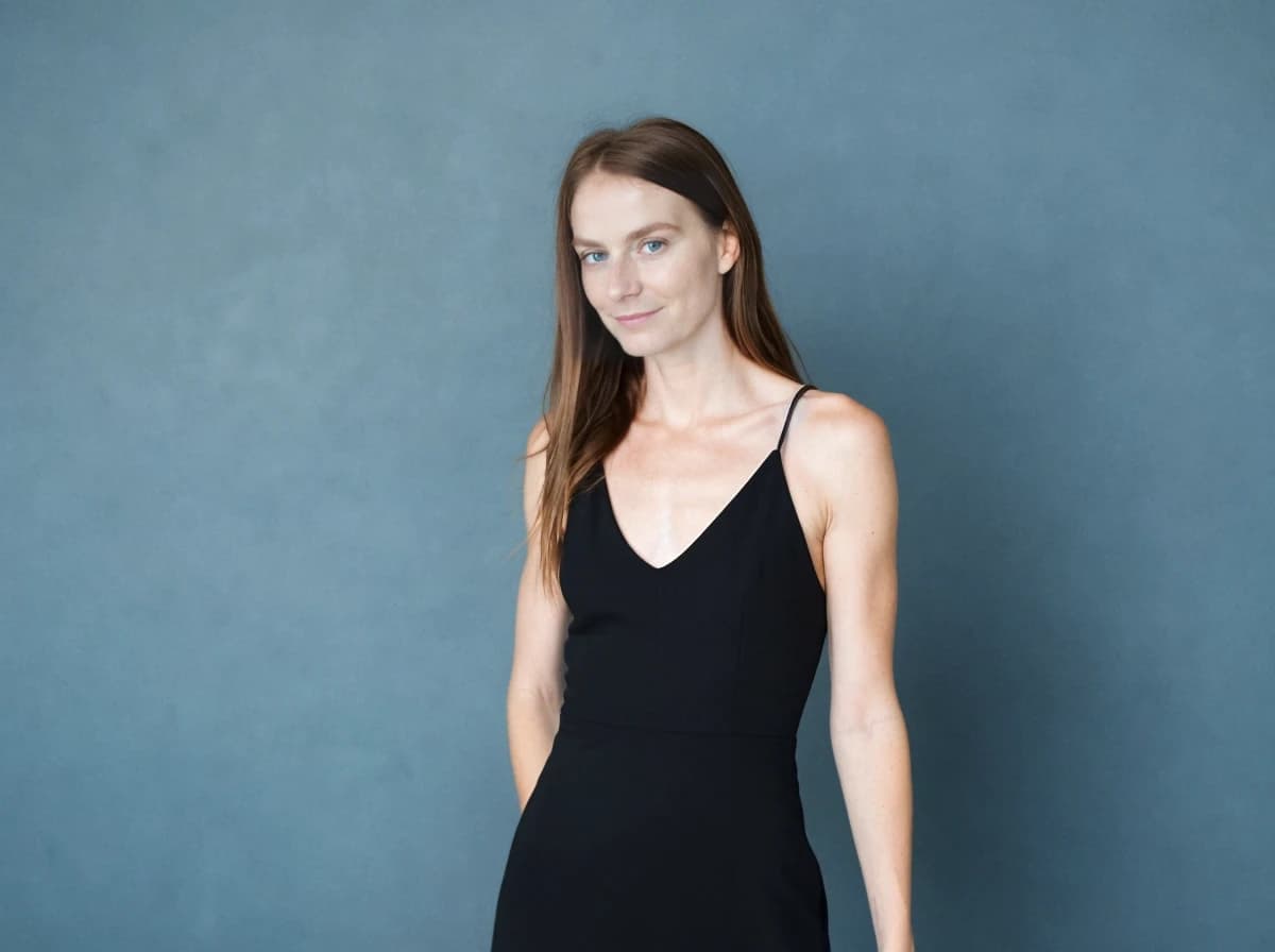 A woman in a black sleeveless dress standing in front of a blue textured background.