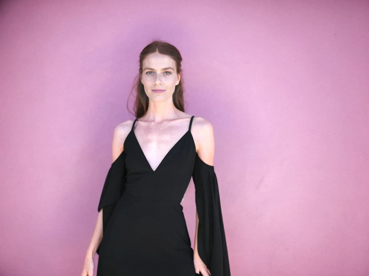 A woman wearing a black dress with cold shoulder sleeves stands against a purple background.