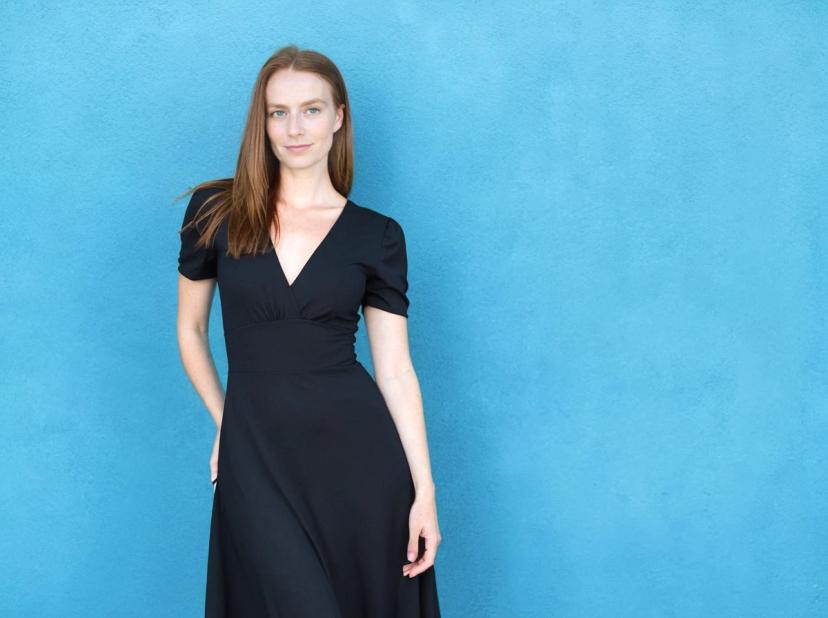 A woman wearing a black V-neck dress standing against a bright blue wall.