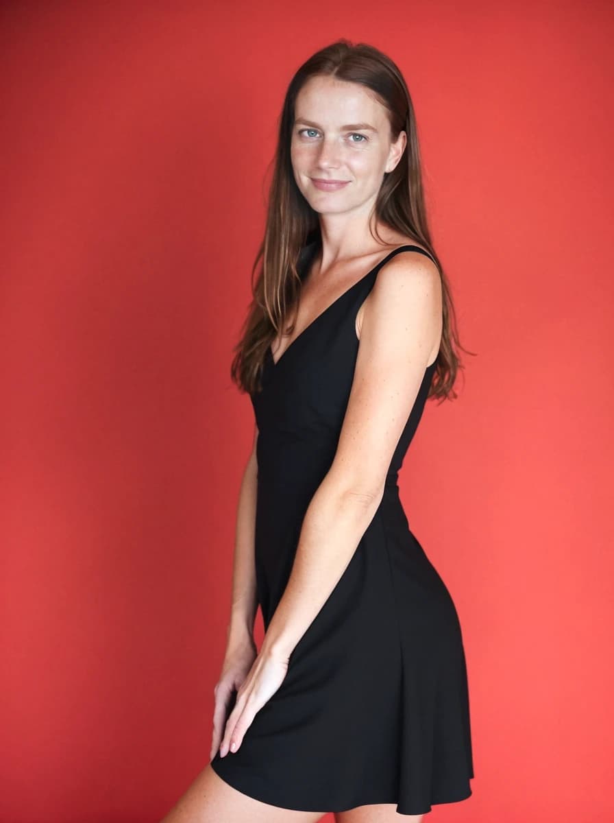 A woman in a black dress with her hand on her hip, standing against a red background.