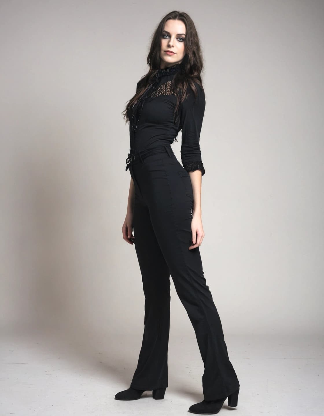 A full-body shot of a young woman with long, dark, wavy hair and dramatic eye makeup. She stands with one leg slightly in front of the other, looking towards the camera, against a plain light gray background. She is wearing a fitted black long-sleeved shirt with lace detailing on the collar and chest, and black flared trousers with black heeled boots.